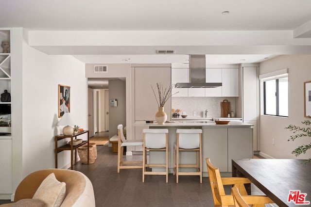 kitchen with dark wood-type flooring, wall chimney exhaust hood, and backsplash