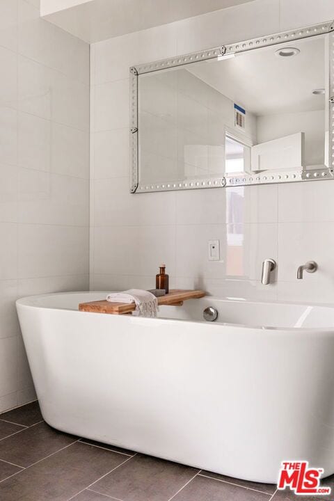 bathroom with tile patterned floors, a bath, and tile walls