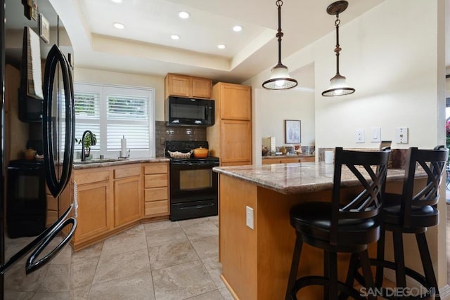 kitchen with sink, decorative light fixtures, a center island, a tray ceiling, and black appliances