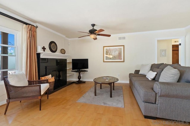 living room featuring ceiling fan, ornamental molding, and light hardwood / wood-style flooring