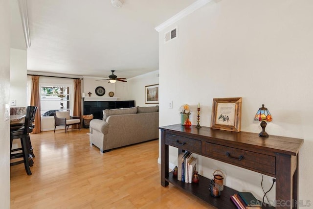 living room with crown molding, ceiling fan, a tiled fireplace, and light hardwood / wood-style flooring