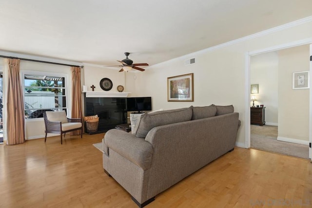 living room featuring crown molding, light hardwood / wood-style floors, a tile fireplace, and ceiling fan