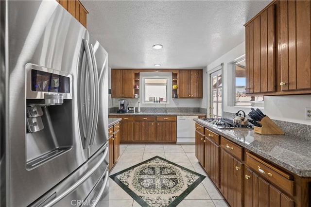 kitchen with appliances with stainless steel finishes, dark stone counters, a textured ceiling, and light tile patterned floors