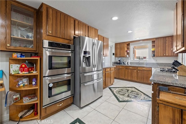 kitchen with light tile patterned floors, sink, stone counters, stainless steel appliances, and a textured ceiling