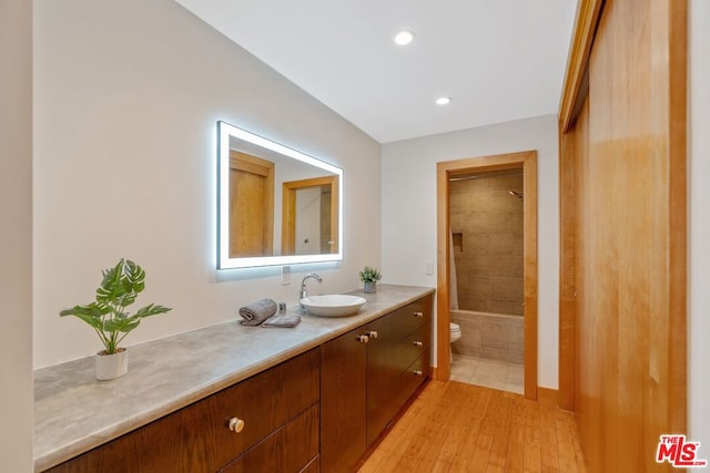 full bathroom featuring tiled shower / bath combo, vanity, wood-type flooring, and toilet