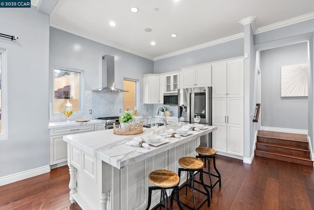 kitchen featuring sink, appliances with stainless steel finishes, white cabinets, a center island with sink, and wall chimney exhaust hood