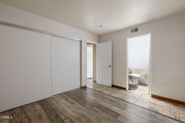 unfurnished bedroom featuring a closet, ensuite bath, and light hardwood / wood-style flooring