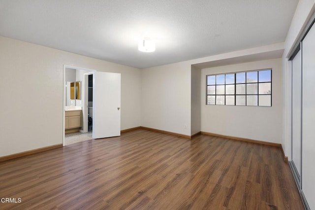 unfurnished bedroom featuring connected bathroom, dark wood-type flooring, and a closet