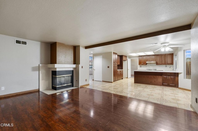 unfurnished living room with a multi sided fireplace, sink, ceiling fan, light hardwood / wood-style floors, and a textured ceiling