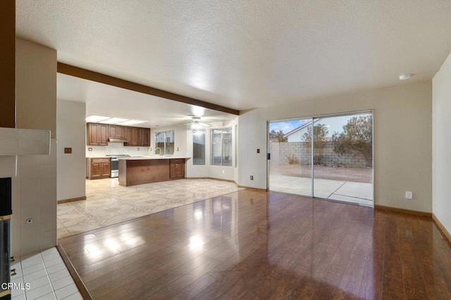 unfurnished living room featuring ceiling fan, sink, light hardwood / wood-style flooring, and a textured ceiling