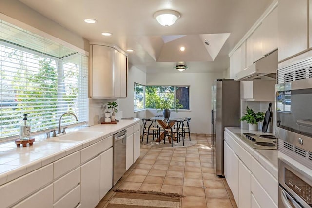 kitchen with sink, tile countertops, appliances with stainless steel finishes, a raised ceiling, and white cabinets