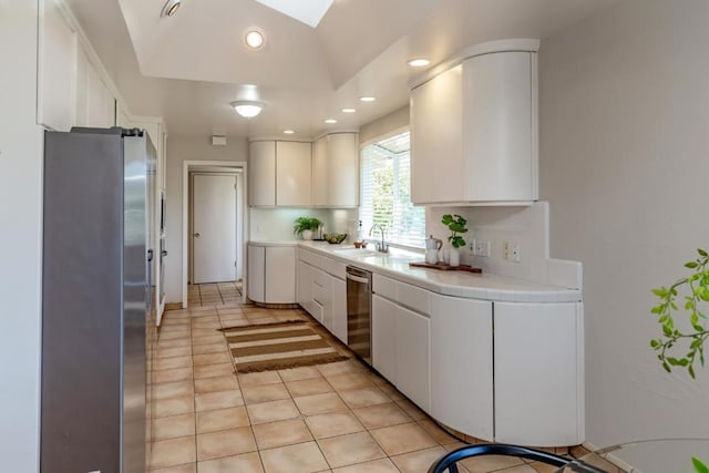 kitchen featuring light tile patterned flooring, lofted ceiling with skylight, sink, white cabinetry, and stainless steel appliances