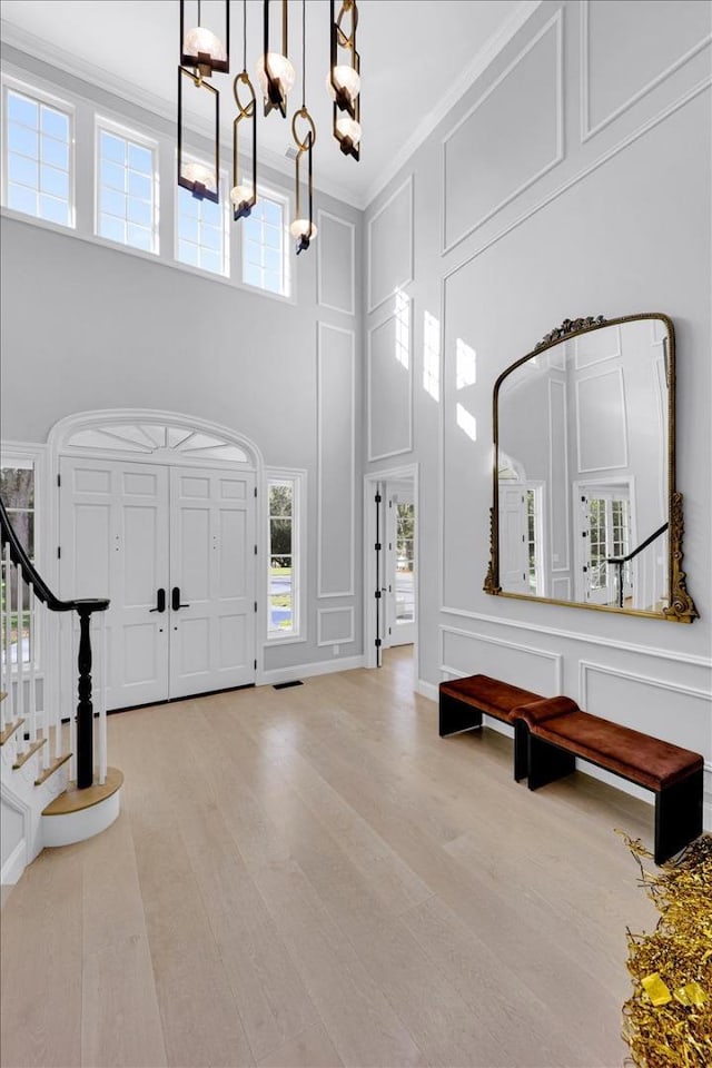 entrance foyer with an inviting chandelier, ornamental molding, light hardwood / wood-style floors, and a high ceiling