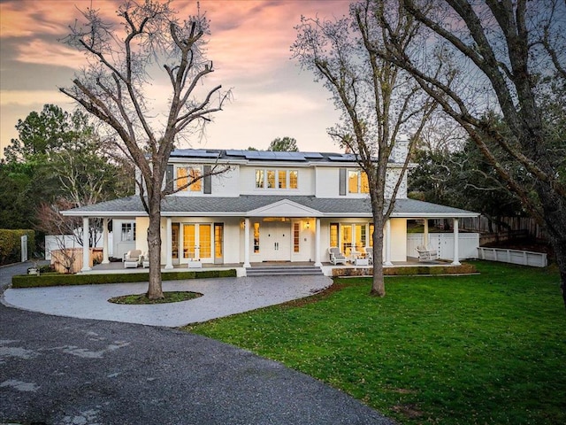 view of front of property featuring a yard, solar panels, and a porch