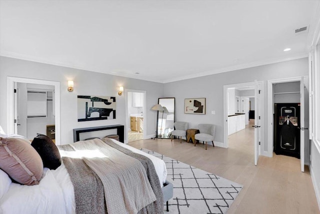 bedroom with crown molding, a walk in closet, connected bathroom, and light wood-type flooring