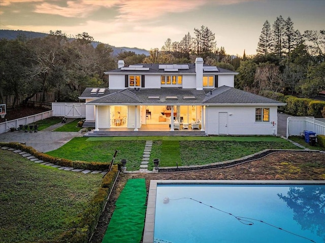 back house at dusk featuring a fenced in pool, a lawn, a patio area, and solar panels