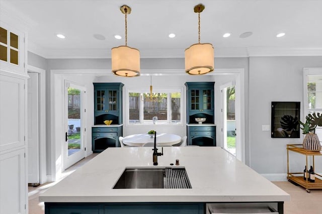 kitchen featuring sink, hanging light fixtures, ornamental molding, an island with sink, and a wealth of natural light