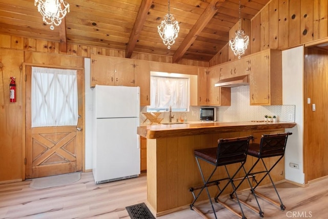 kitchen featuring a breakfast bar area, kitchen peninsula, hanging light fixtures, and white fridge