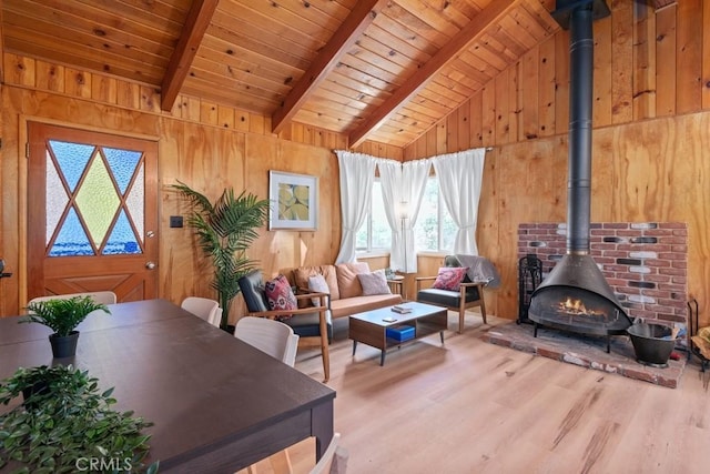 living room with a wood stove, vaulted ceiling with beams, wooden ceiling, and wooden walls