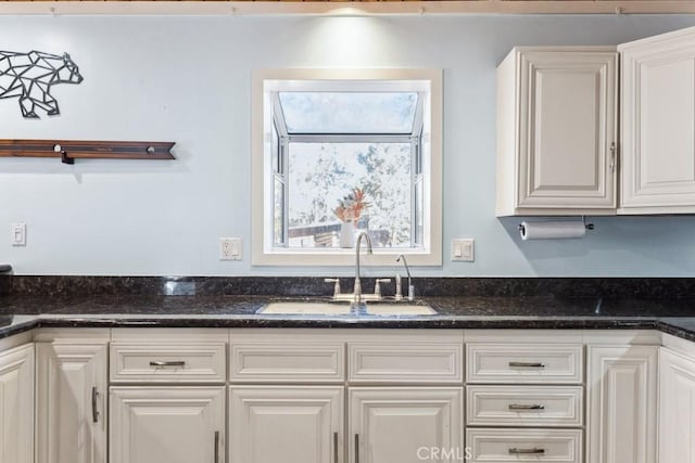 kitchen featuring white cabinetry, dark stone counters, and sink