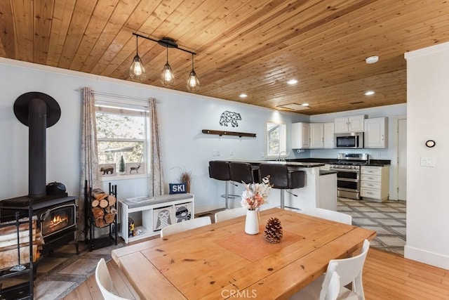 dining room with light hardwood / wood-style flooring, a wealth of natural light, a wood stove, and wooden ceiling