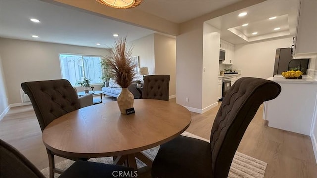 dining area featuring a raised ceiling and light hardwood / wood-style flooring