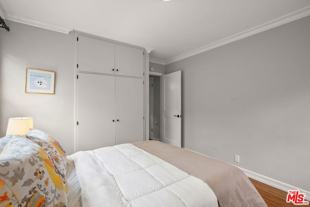 bedroom with dark wood-type flooring, ornamental molding, and a closet