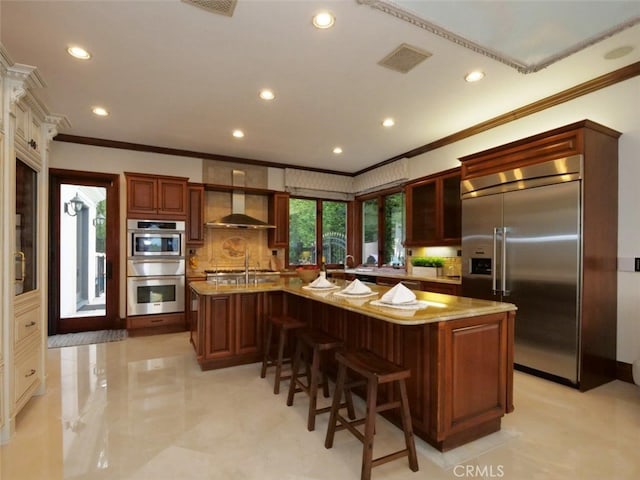 kitchen featuring stainless steel appliances, an island with sink, wall chimney range hood, and crown molding