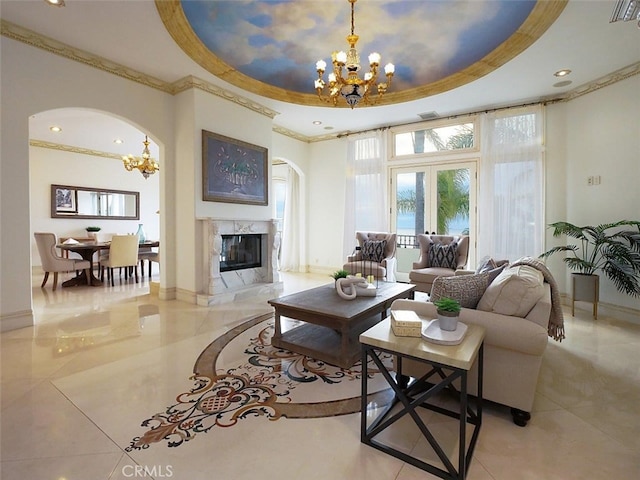 living room with an inviting chandelier, ornamental molding, a high end fireplace, and a tray ceiling