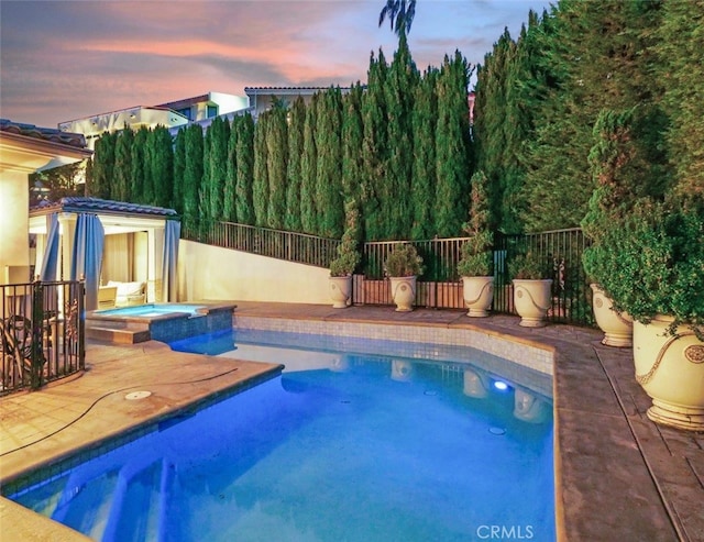 pool at dusk with an in ground hot tub and a patio area