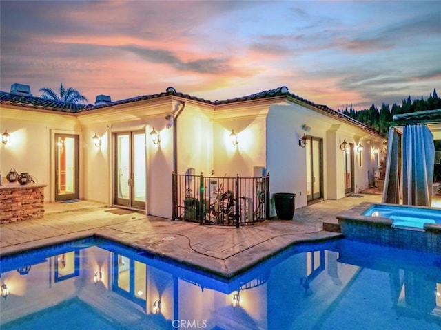 pool at dusk with an in ground hot tub, a patio, and french doors