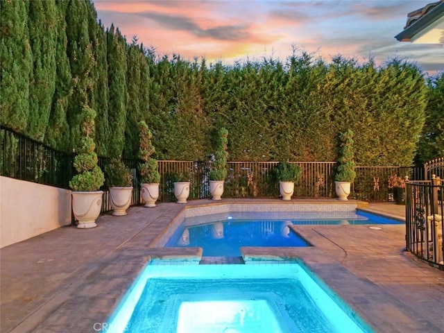 pool at dusk featuring a patio area and an in ground hot tub