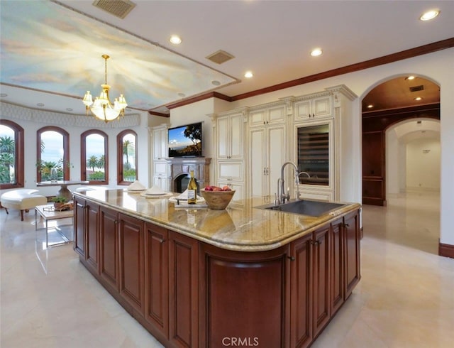 kitchen with pendant lighting, sink, a large island with sink, light stone counters, and cream cabinetry