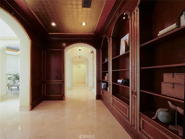 hallway with built in shelves, ornamental molding, and a tray ceiling