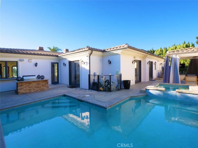 back of property with a swimming pool with hot tub, a patio area, and exterior bar