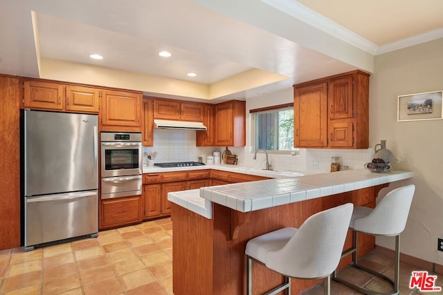 kitchen featuring backsplash, a kitchen breakfast bar, tile counters, kitchen peninsula, and stainless steel appliances