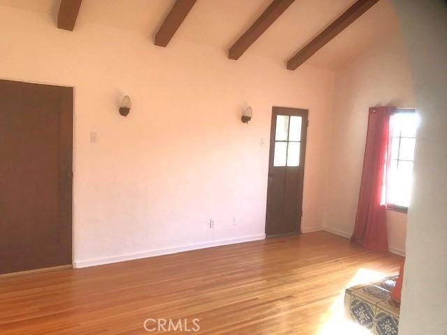 spare room featuring lofted ceiling with beams, plenty of natural light, and light hardwood / wood-style floors