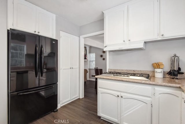 kitchen featuring stainless steel gas stovetop, black fridge, dark wood-type flooring, and white cabinets