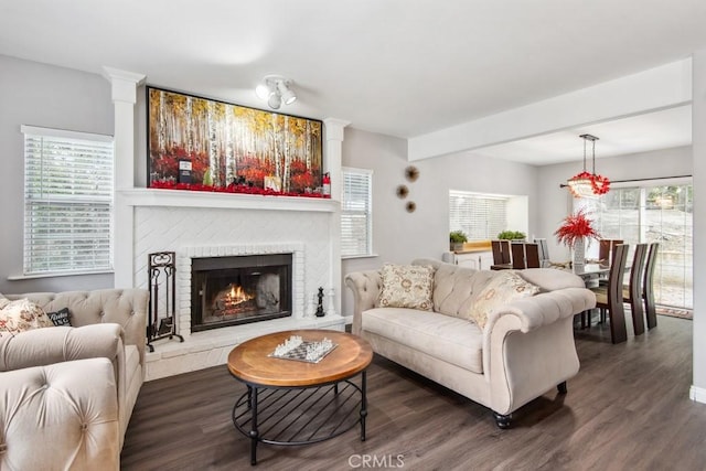 living room with a brick fireplace and dark wood-type flooring