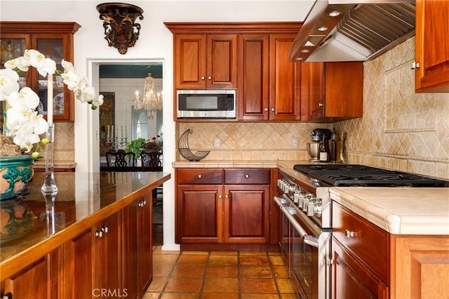 kitchen with dark tile patterned floors, backsplash, stainless steel appliances, extractor fan, and tile countertops