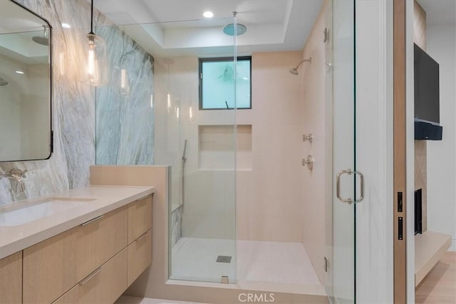 bathroom with vanity, a tray ceiling, a shower with shower door, and tasteful backsplash