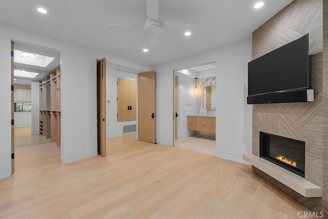 unfurnished living room featuring a large fireplace, ceiling fan, and light hardwood / wood-style flooring