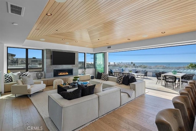 living room with wood ceiling, a fireplace, a raised ceiling, and light hardwood / wood-style floors