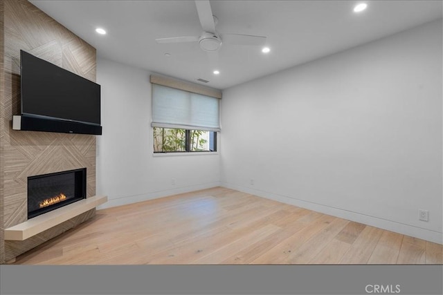 unfurnished living room featuring a large fireplace, ceiling fan, and light wood-type flooring