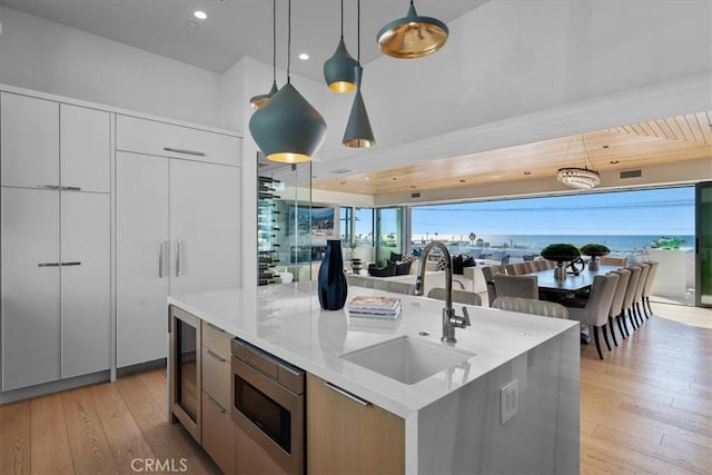 kitchen featuring sink, hanging light fixtures, stainless steel microwave, an island with sink, and white cabinets