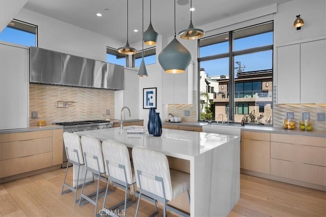 kitchen featuring a breakfast bar, decorative light fixtures, ventilation hood, stainless steel stove, and a kitchen island with sink