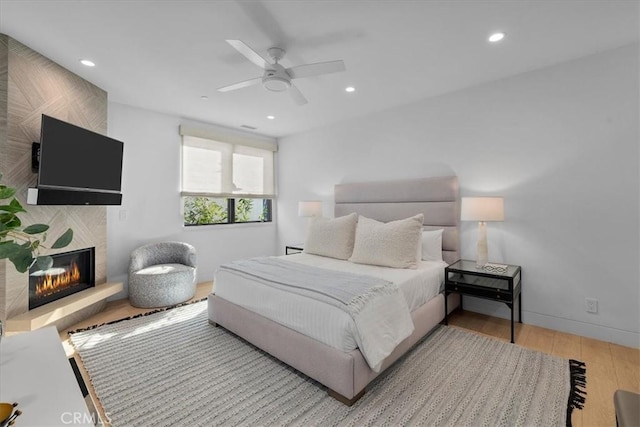 bedroom with a large fireplace, ceiling fan, and light wood-type flooring