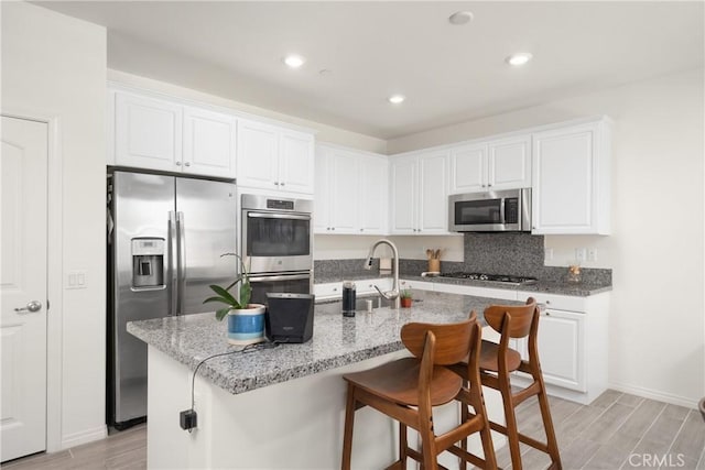 kitchen with an island with sink, white cabinetry, a breakfast bar area, light stone counters, and stainless steel appliances