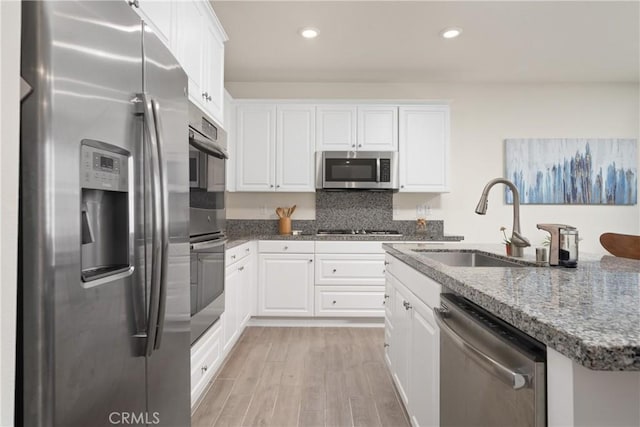 kitchen with sink, white cabinetry, dark stone counters, light wood-type flooring, and stainless steel appliances