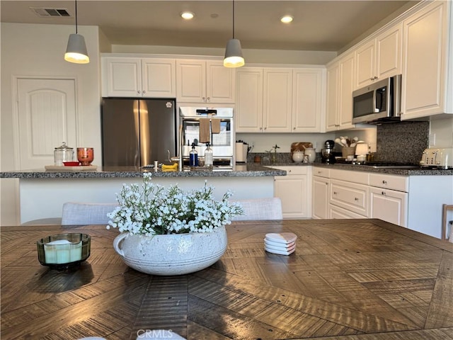 kitchen with white cabinetry, dark stone countertops, pendant lighting, stainless steel appliances, and backsplash